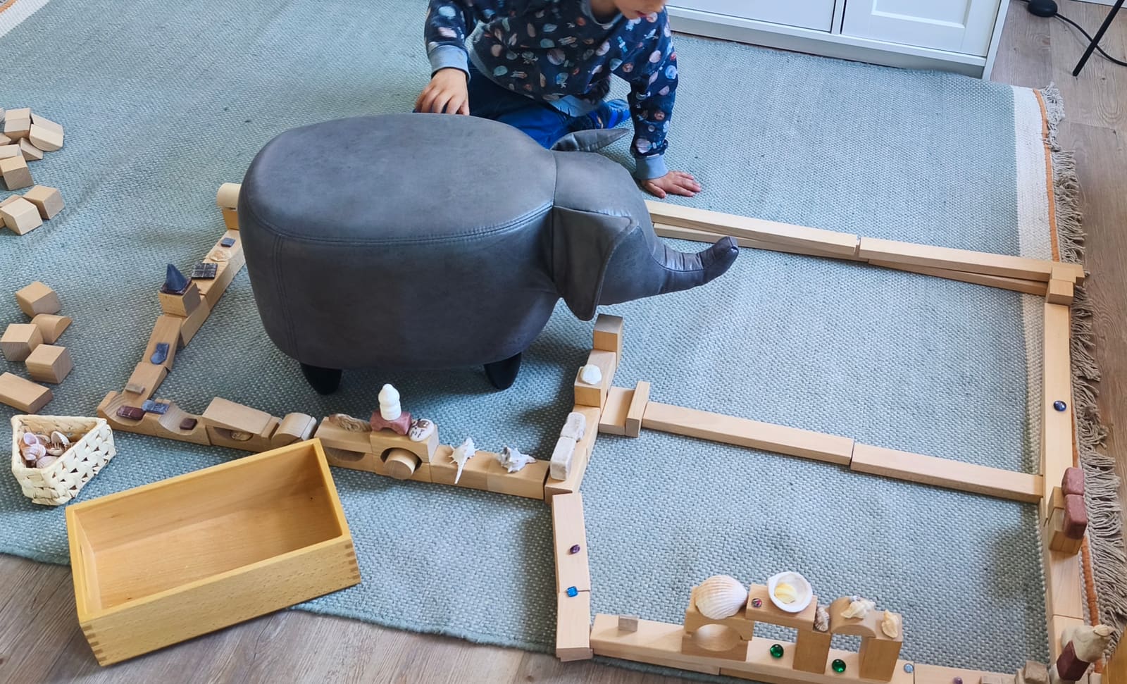 Freispiel auf dem Teppich: ein Kind baut mit Holzbausteinen ein großes Gehege